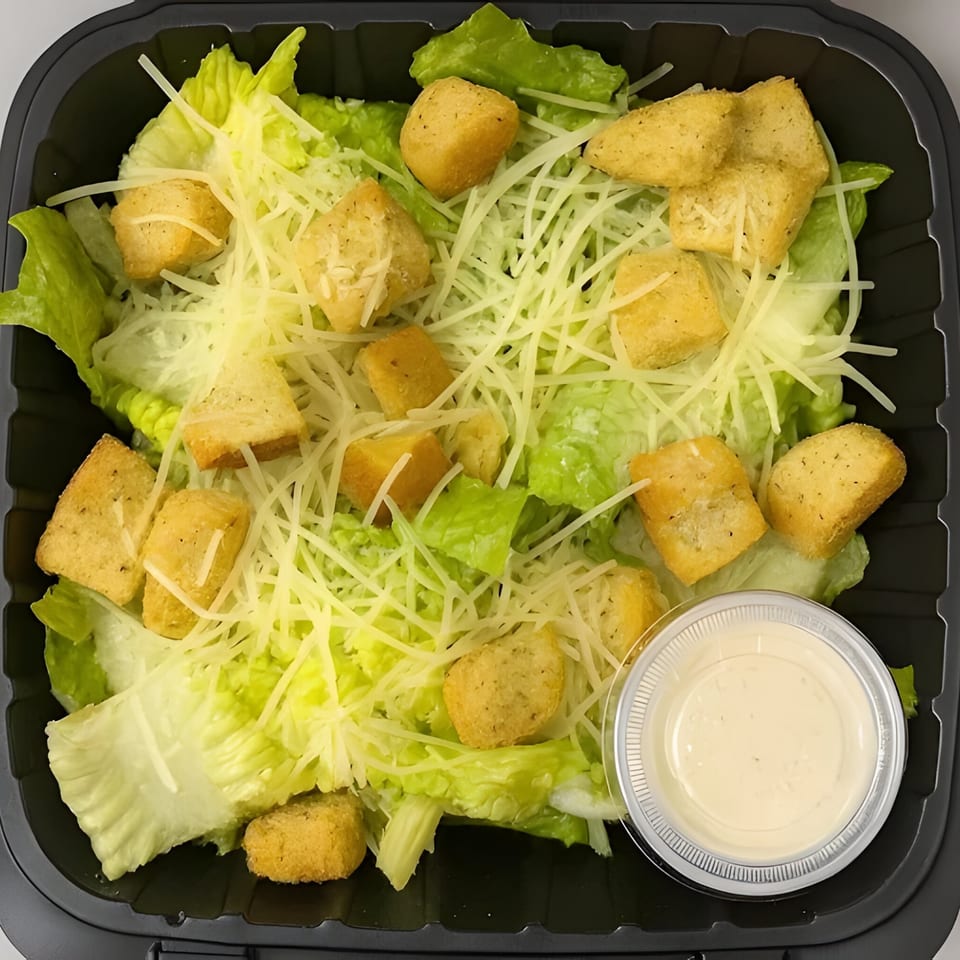 Caesar salad with fresh romaine lettuce, shredded Parmesan cheese, croutons, and a side of dressing.