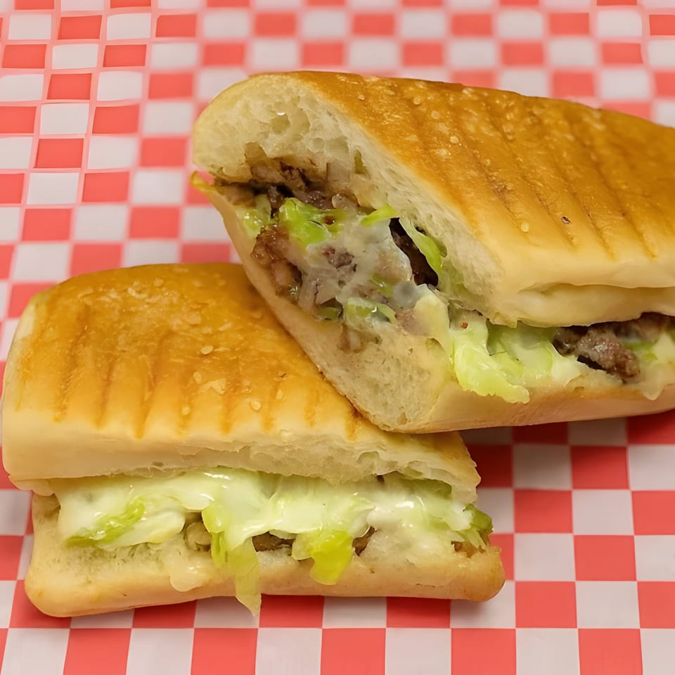 Two halves of a Halal Philly cheesesteak sandwich with meat, cheese, and lettuce on a red and white checkered paper.